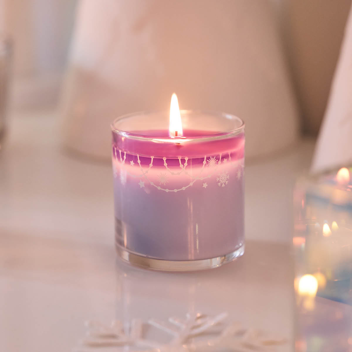Snowflakes & Cotton Mini Jar Candle shown lit against a light background and a light surface.