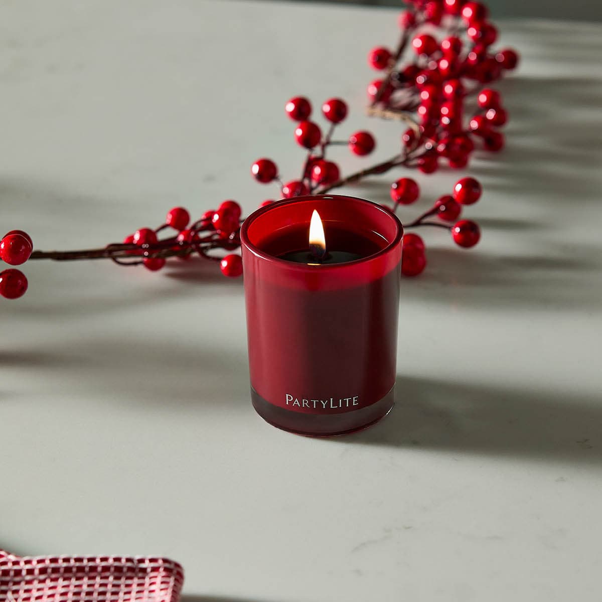 Bourbon Cherry Escential Jar Candle lit on a light surface with red fairy lights behind it.