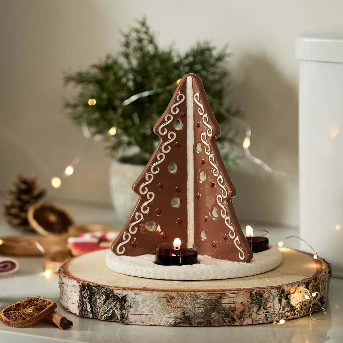 Gingerbread Tree Tealight Holder with lit tealights on a wooden round log inspired coaster, surrounded by fairy lights.
