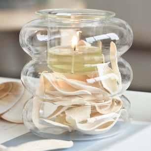 Illusion Tealight Holder with a lit candle and decorative wood chippings with a star shaped item on a white table top.