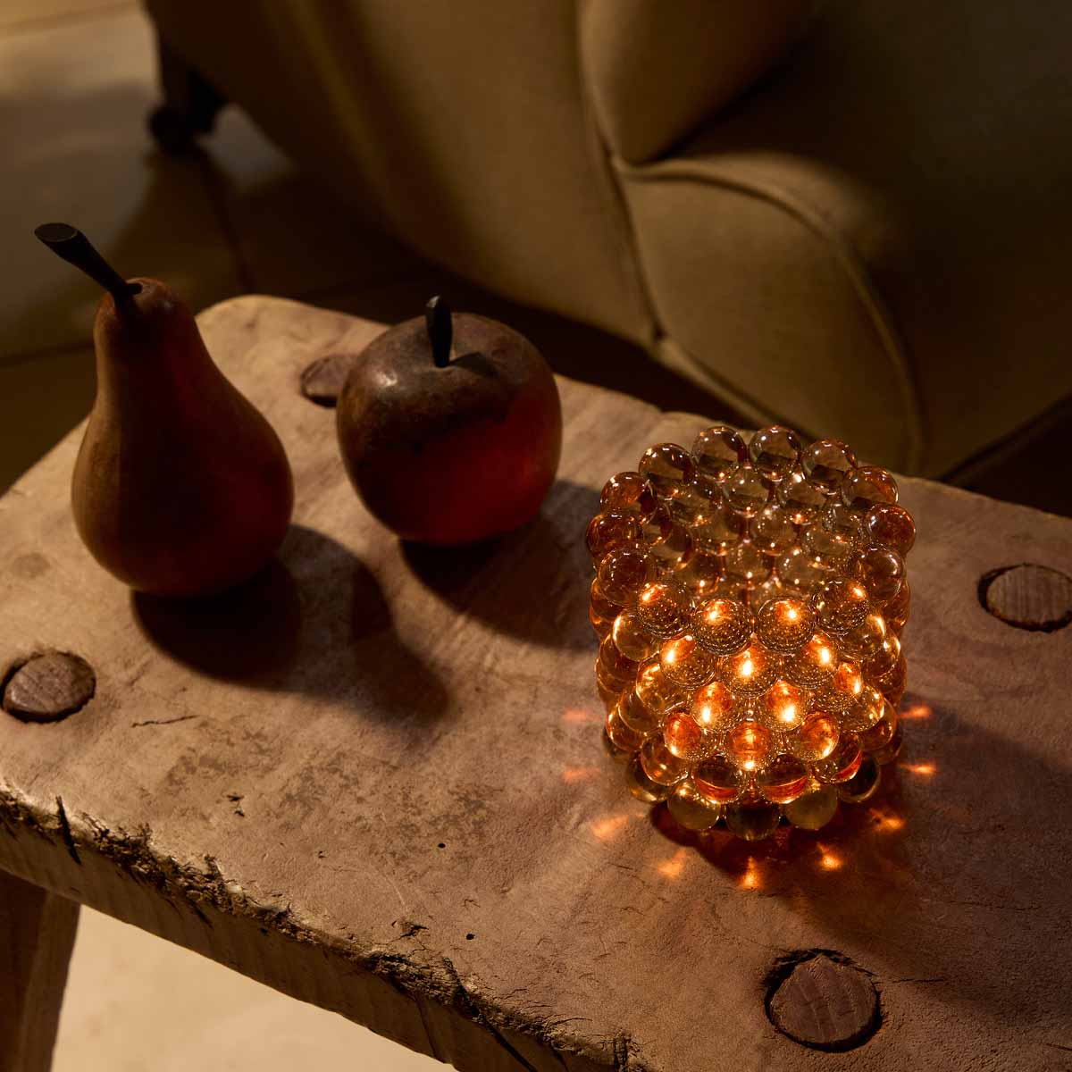 Glass Bead Tealight Holder lit on a wooden table next to decorative fruit items.