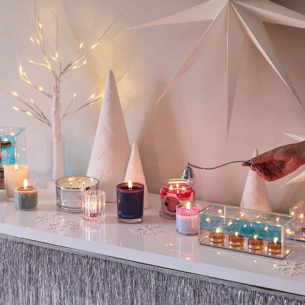 An assortment of colorful various jar candles from Escentail Jar candle, Mini Jar candle, 3-wick Jar candle, 3-wick Ripple Jar Candle and a clear Tealight holder with four lit tealights against a Christmas themed background.