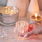 Ripple Glass Tealight/Votive Holder Pair shown with a lit tealight with a Silver Ripple 3-wick Jar Candle and Mini Jar Candle on  light surface with a decorative snowflake.