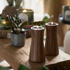 Faux Bois Tealight Holder Pair with lit tealight candles on a wooden surface with a plant in the background.