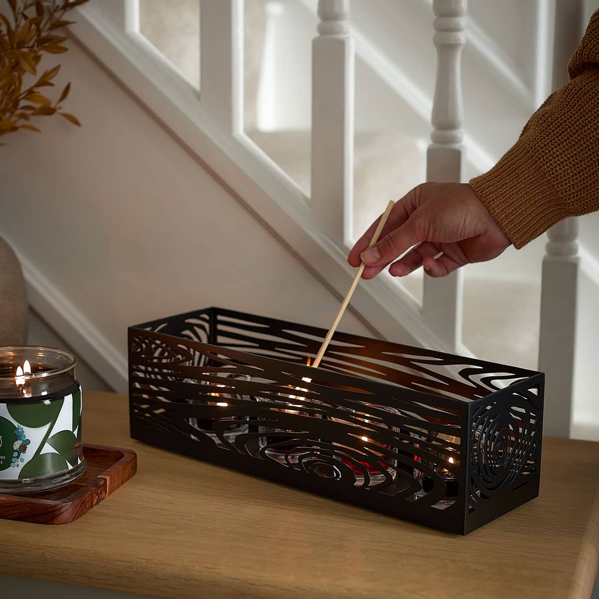 Wood Grain Centerpiece with candles being lit by a long matchstick on a wooden surface and white bannisters of stairs in the background.