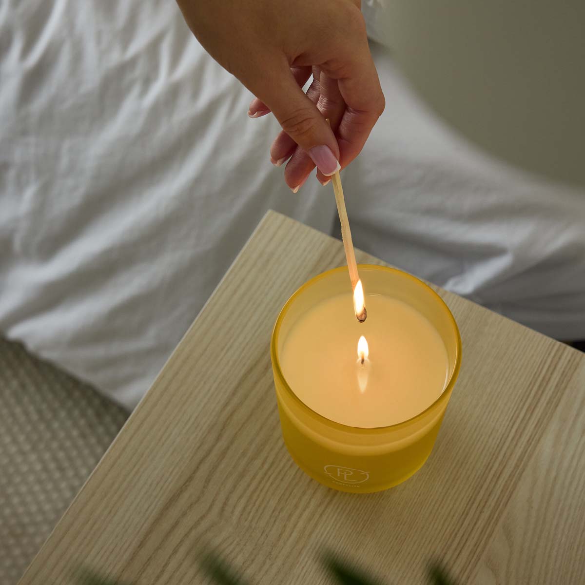 Coastal Amber & Shea Refillable Jar Candle being lit by a long match being held in a lady's fingers on a wooden surface.