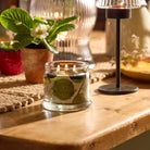Farm Fresh Herbs 3-Wick Jar Candle lit on a wooden table top with plant in behind it.