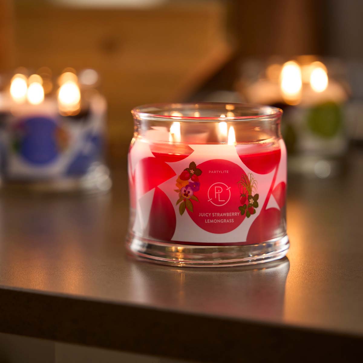 Juicy Strawberry Lemongrass 3-wick Jar Candle lit on a wooden surface.