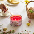 Garden Party 4-Wick Jar Candle being lit by a long match, beside a basket of Easter Eggs on a white table cloth.