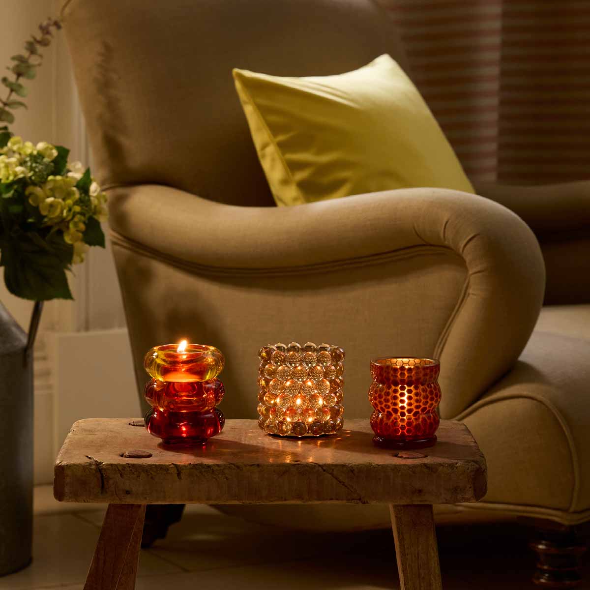 Honeycomb Tealight/ Votive Holder with lit candle next to other Tealight holders on a wooden table beside a armchair.
