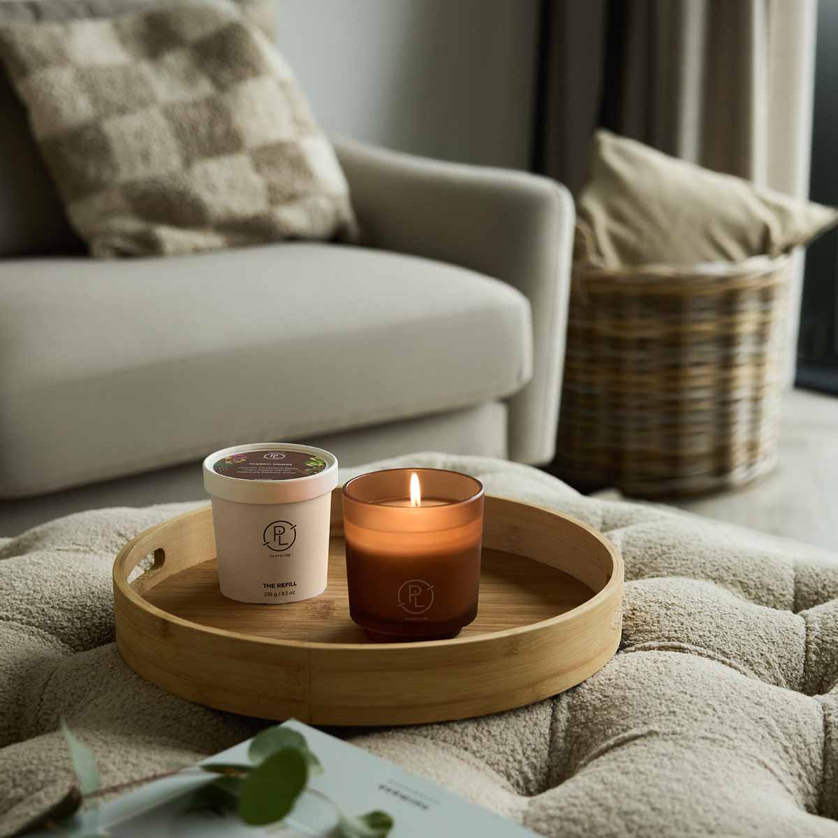 Tamboti Woods Candle Refill shown with the Refillable Tamboti Woods Jar candle on a wooden tray on soft furnishings with a sofa in the background.