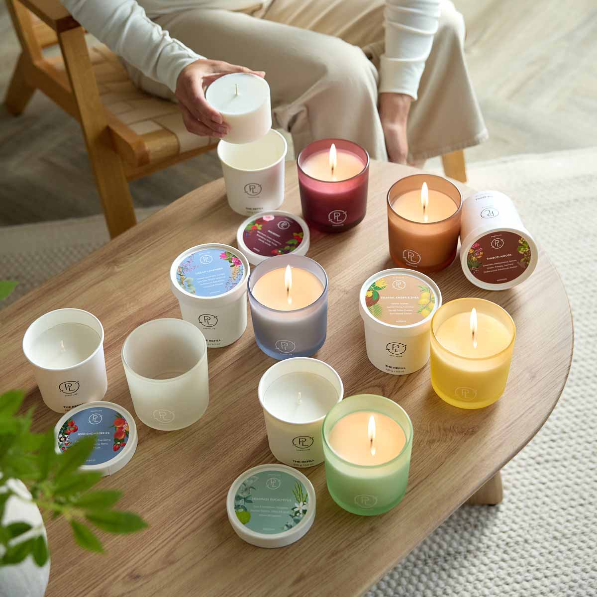 Assortment of Refillable Jar candles shown with Wax Refills on a wooden table with a person in the background, holding one of the wax refills.