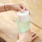 Iced Snowberries wax refill shown being inserted into a refill jar by a lady's hands on a wooden surface.