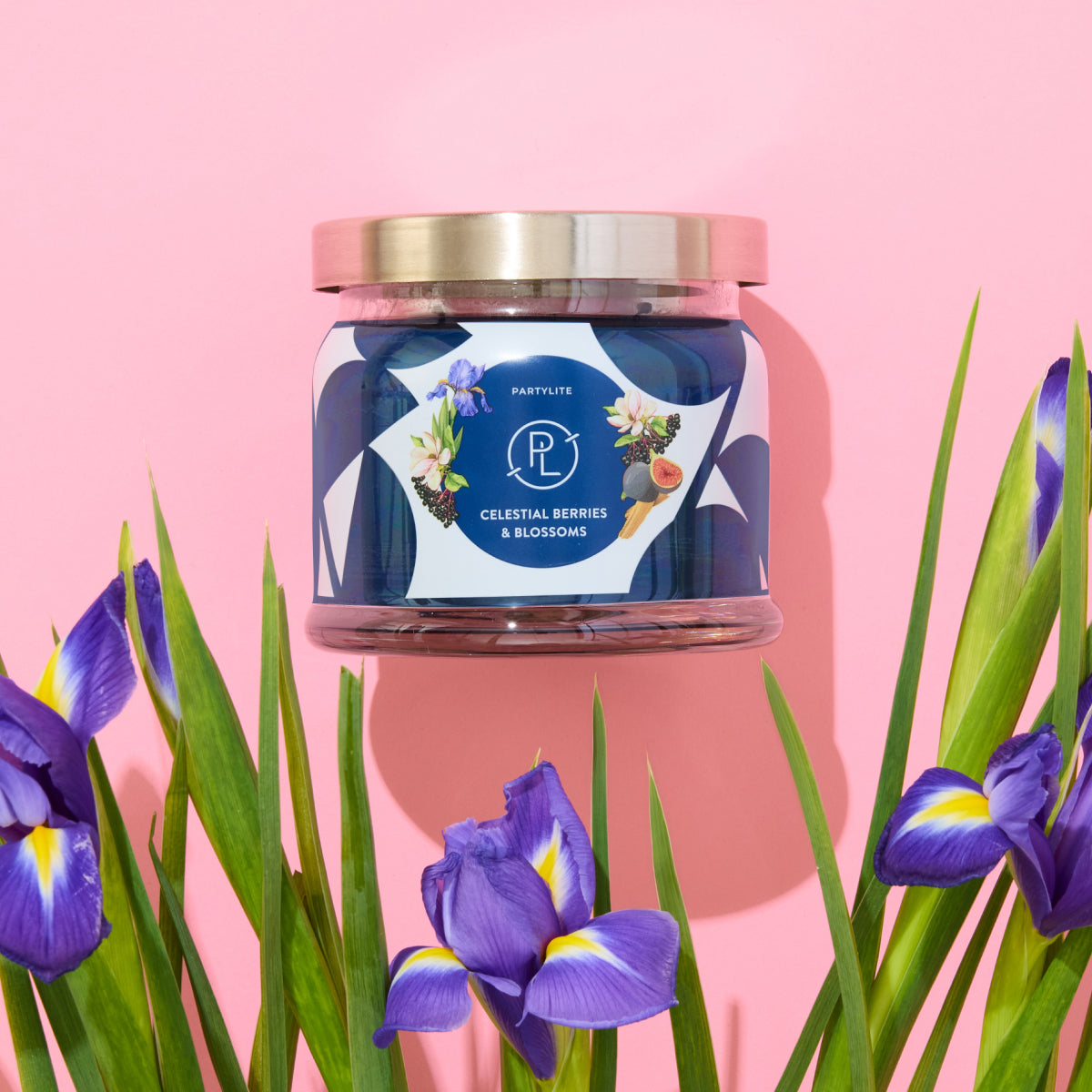 Celestial Berries and Blossoms blue 3-wick jar candle against a pink background with colourful flowers.