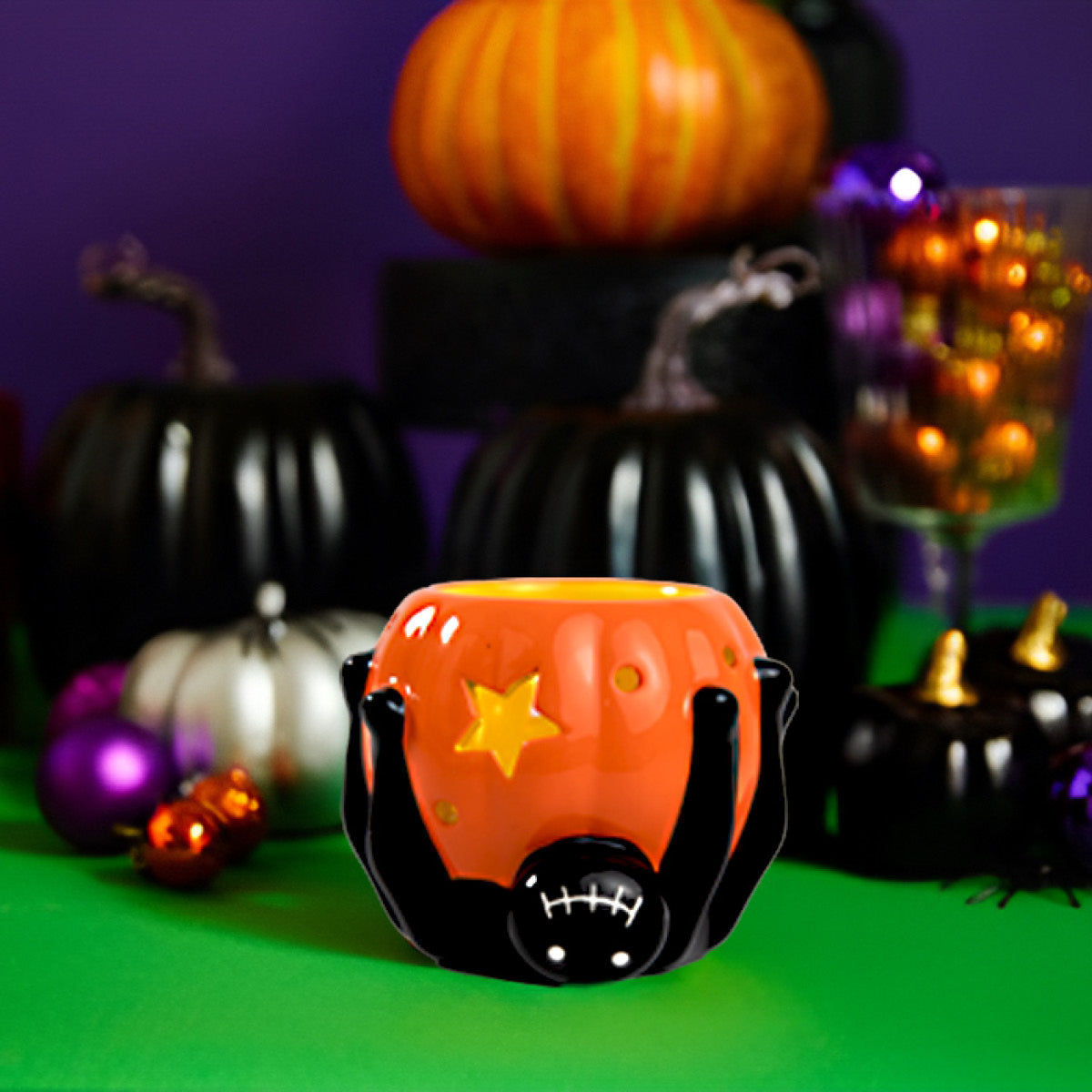 Silly Spider TealightVotive holder black spider and orange cup set a green surface with purple background and lots of Halloween decorative items in black, silver and purple and orange