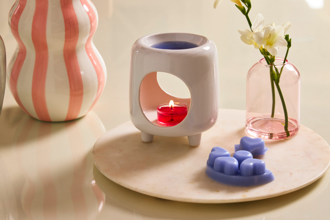 Mini Chiminea wax warmer with a red tealight candle, surrounded by Scent Plus Melts and decorative items on a light surface.