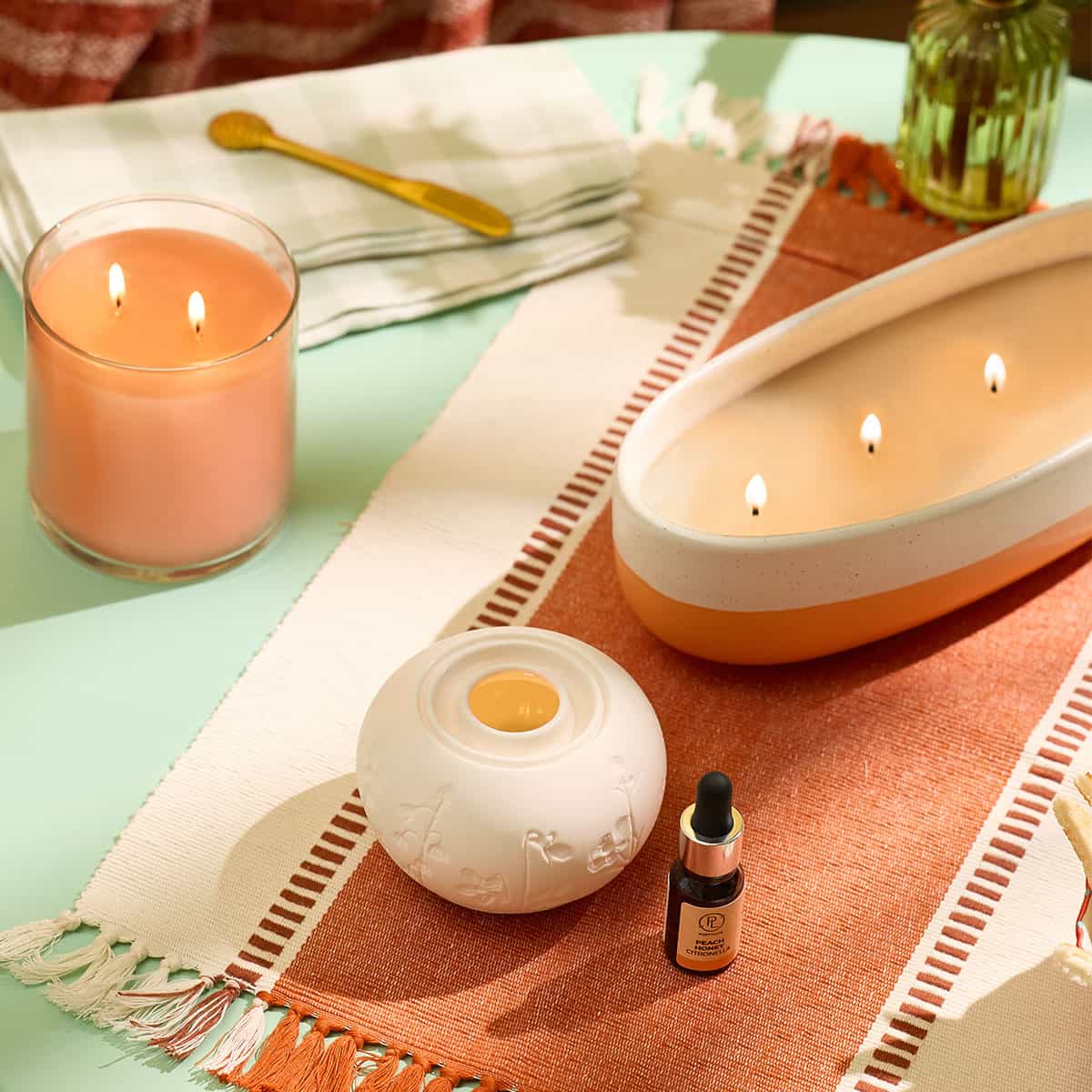 Illuminescents Blooming Fields Fragrance Warmer with Citronella oil shown with a GloLite Citronella 2-wick jar candle and a ceramic 4-wick two tone jar candle on a woven table mat on a green colored table
