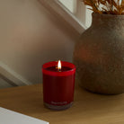 Autumn Sangria Escential Jar lit on a wooden surface with a vase in the background.