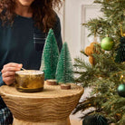 Whiskey & Oak 3-Wick Ripple Jar Candle being lit by a lady with a long match stick on a wooden surface with a Christmas theme background.