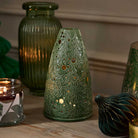 Lacy Greens Tealight Holder shown with a lit tealights and a lit 3-wick jar candle beside it on a wooden surface.