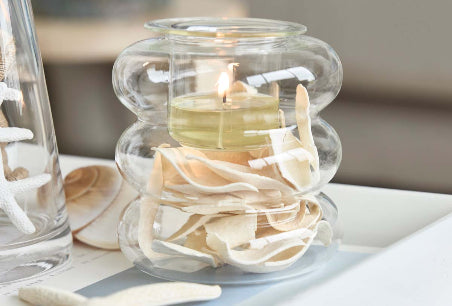 Illusion Tealight Holder with a lit candle and decorative wood chippings with a star shaped item on a white table top.