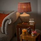 Pistachio Biscotti Escential Jar Candle lit on a side table with the 3-wick candle and another table showing a lamp and part of a sofa.
