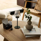 Modern Farmhouse Tealight Lamp shown with a box of open tealights on a wooden table with a chair in the background.