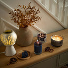 Nordic Air Escential Jar Candle lit shown with a 3-wick Jar candle, a 3-wick Ripple Jar candle and a scent glow warmer with a ceramic vase of leaves on a wooden surface.