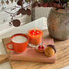Acorn Tealight Holder Pair shown with a lit 3-wick Jar Candle with an orange cup on a wooden surface.