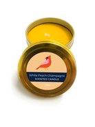 Scented candle in a gold tin with a label featuring a cardinal and 'White Peach Champagne' text on a white background.