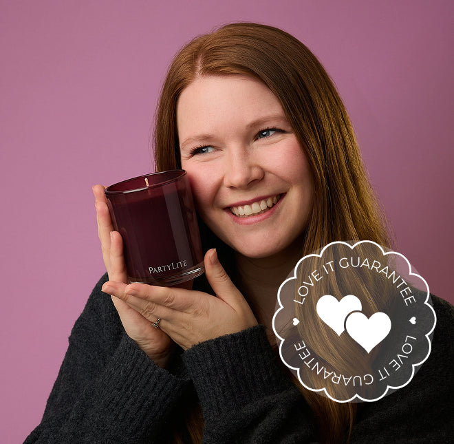 Woman holding a Party Lite candle with a 'Love It Guarantee' badge on a pink background