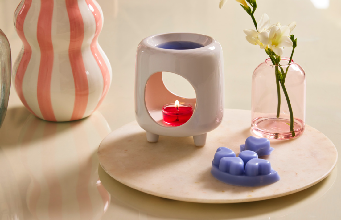 Mini Chiminea wax warmer with a red tealight candle, surrounded by Scent Plus Melts and  decorative items on a light surface.