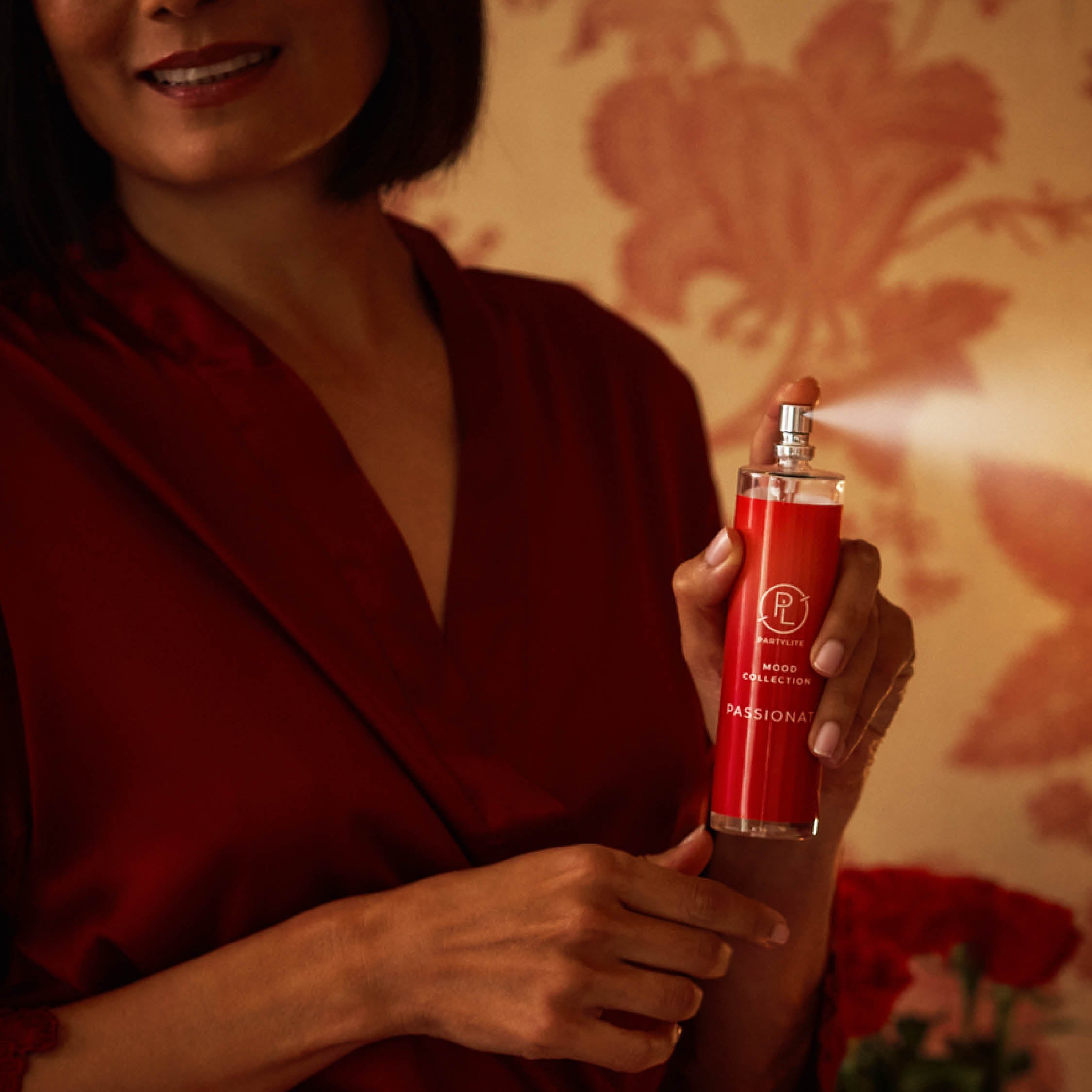 Woman holding a red room spray bottle Passionate by Mood Collection with a floral background.