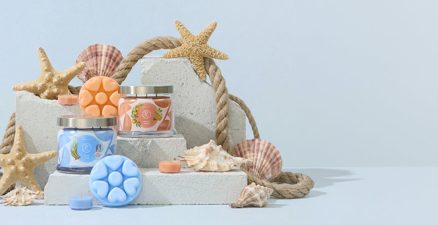 Seaside Escape Collection featuring Yacht Club Fragrance, 3-wick jar candle, heart shaped wax melts and a single tealight, with Seaside Neroli Fragrance, 3-wick jar candle, heart shaped wax melts and a single tealight, shown with star fish shapes and sea shells and a beige rope.