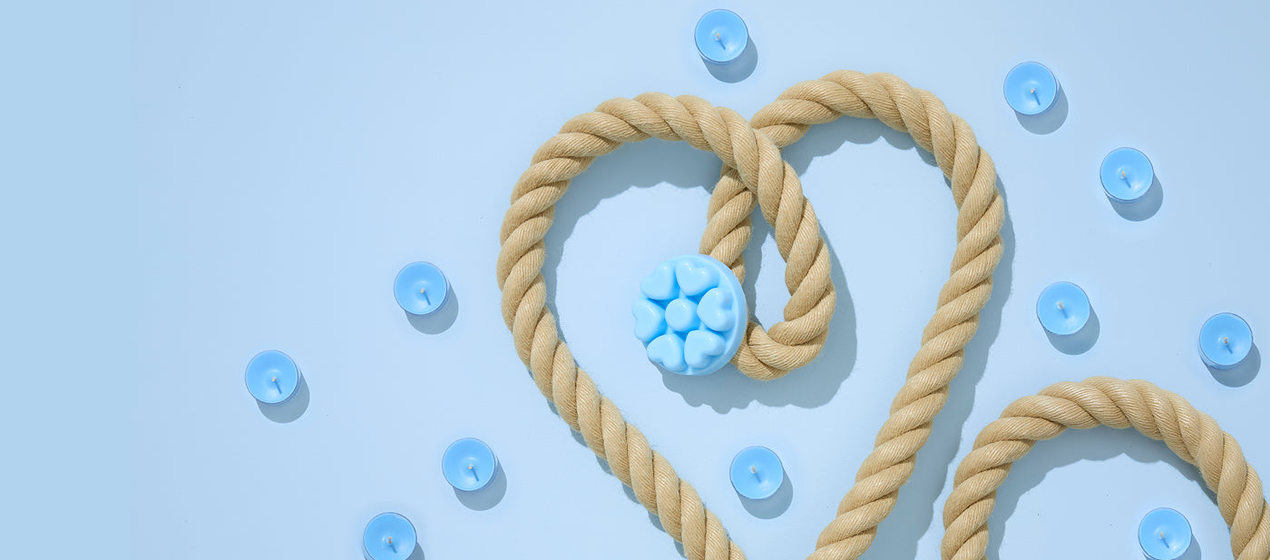 Yacht Club fragrance, blue scattered tealights with blue heart shaped melts with a beige rope against a pale blue background.