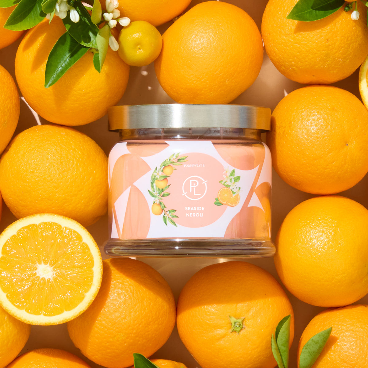 Candle jar with decorated label featuring oranges and blossoms with oranges surrounding. 