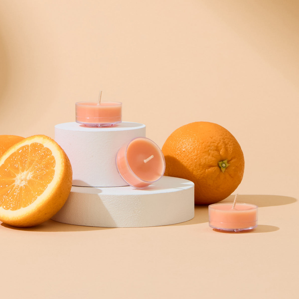 Light orange tealights on round white stands with oranges with a light orange background.