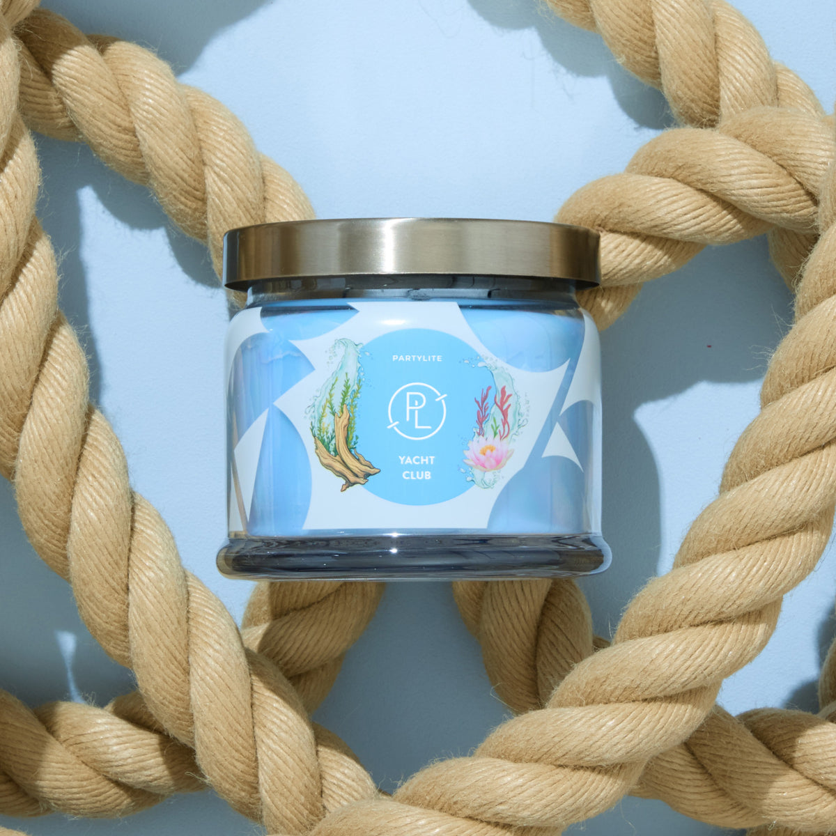 Candle jar with blue label with beige rope behind and a light blue background. 